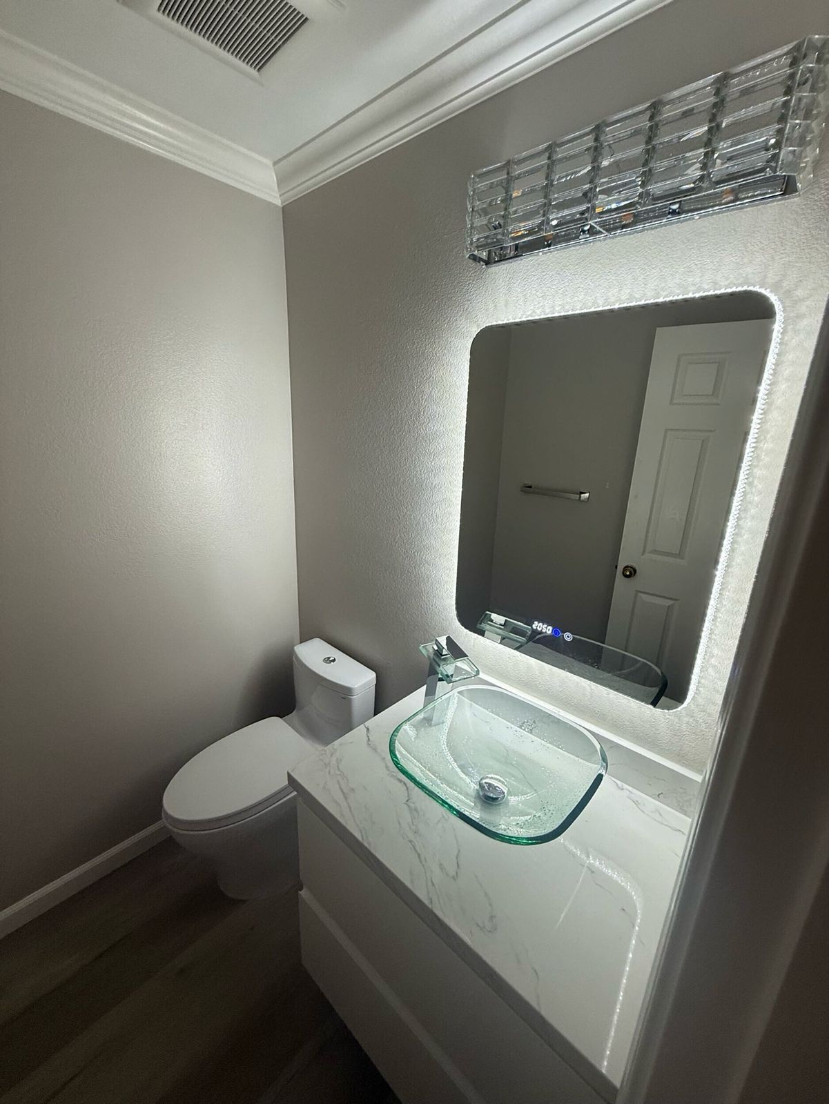 Contemporary bathroom remodel featuring a sleek white floating vanity with under-mount sink, frameless mirror with modern LED lighting, walk-in shower with glass sliding doors and marble-look porcelain tiles, and gray floor tiles with subtle veining — project by Dream Build Services in the Bay Area.