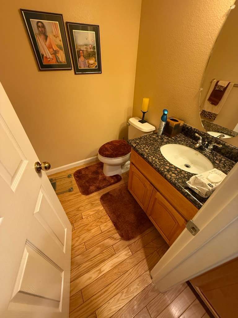 Small bathroom with white toilet, wood vanity, granite countertop, and wall art.