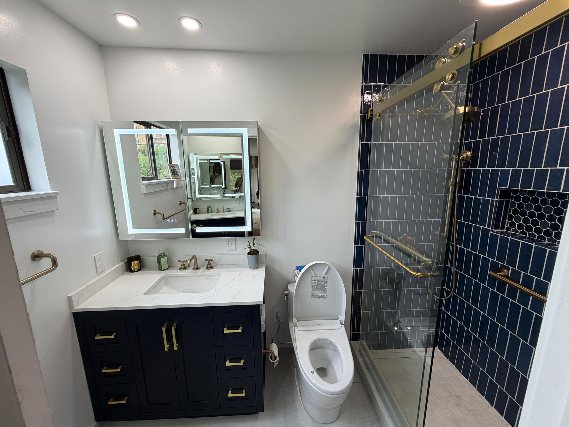 Complete bathroom renovation transforming an outdated bathtub into a spacious, modern walk-in shower with frameless glass enclosure, custom navy blue subway tile, decorative shower niche, brushed brass fixtures, rainfall showerhead, handheld shower system, built-in shower bench, grab bars for accessibility, and premium porcelain tile flooring. The remodel also features a custom navy shaker vanity with quartz countertop, integrated LED medicine cabinet, modern undermount sink, upgraded lighting, comfort-height smart toilet, and contemporary plumbing fixtures.
This bathroom remodel was designed to improve functionality, accessibility, storage, durability, and everyday comfort while adding lasting value to the home. Dream Build Services specializes in custom bathroom renovations using high-quality materials and craftsmanship tailored to each homeowner's style and needs.
Services Included:
• Bathroom Remodeling
• Bathroom Renovation
• Tub-to-Shower Conversion
• Walk-In Shower Installation
• Custom Tile Installation
• Frameless Glass Shower
• Quartz Countertop Installation
• Custom Vanity Installation
• LED Medicine Cabinet Installation
• Accessibility Bathroom Upgrades
• Plumbing Fixture Replacement
• Home Remodeling
• General Contractor Services