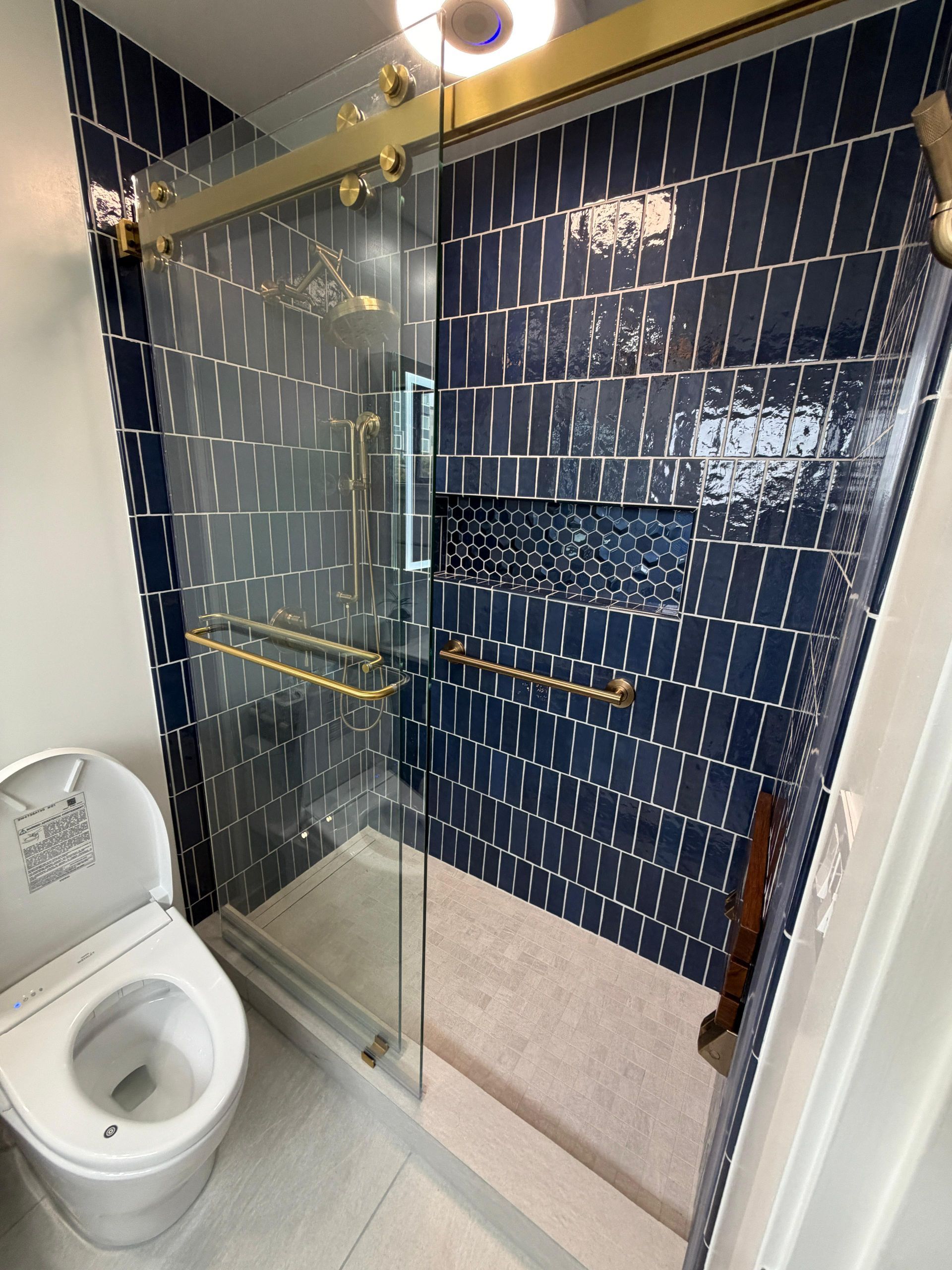 Complete bathroom renovation transforming an outdated bathtub into a spacious, modern walk-in shower with frameless glass enclosure, custom navy blue subway tile, decorative shower niche, brushed brass fixtures, rainfall showerhead, handheld shower system, built-in shower bench, grab bars for accessibility, and premium porcelain tile flooring. The remodel also features a custom navy shaker vanity with quartz countertop, integrated LED medicine cabinet, modern undermount sink, upgraded lighting, comfort-height smart toilet, and contemporary plumbing fixtures.
This bathroom remodel was designed to improve functionality, accessibility, storage, durability, and everyday comfort while adding lasting value to the home. Dream Build Services specializes in custom bathroom renovations using high-quality materials and craftsmanship tailored to each homeowner's style and needs.
Services Included:
• Bathroom Remodeling
• Bathroom Renovation
• Tub-to-Shower Conversion
• Walk-In Shower Installation
• Custom Tile Installation
• Frameless Glass Shower
• Quartz Countertop Installation
• Custom Vanity Installation
• LED Medicine Cabinet Installation
• Accessibility Bathroom Upgrades
• Plumbing Fixture Replacement
• Home Remodeling
• General Contractor Services