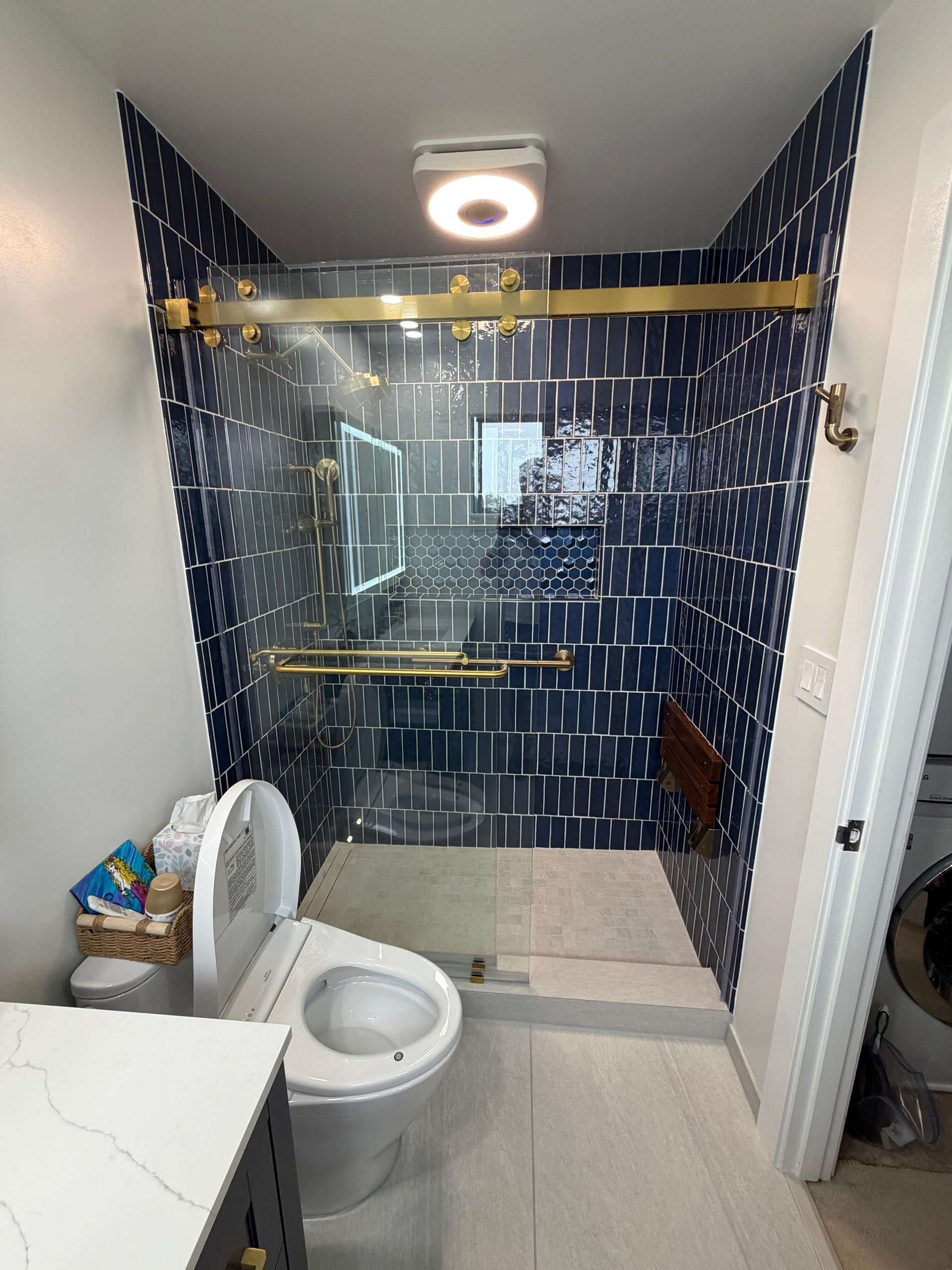 Complete bathroom renovation transforming an outdated bathtub into a spacious, modern walk-in shower with frameless glass enclosure, custom navy blue subway tile, decorative shower niche, brushed brass fixtures, rainfall showerhead, handheld shower system, built-in shower bench, grab bars for accessibility, and premium porcelain tile flooring. The remodel also features a custom navy shaker vanity with quartz countertop, integrated LED medicine cabinet, modern undermount sink, upgraded lighting, comfort-height smart toilet, and contemporary plumbing fixtures.
This bathroom remodel was designed to improve functionality, accessibility, storage, durability, and everyday comfort while adding lasting value to the home. Dream Build Services specializes in custom bathroom renovations using high-quality materials and craftsmanship tailored to each homeowner's style and needs.
Services Included:
• Bathroom Remodeling
• Bathroom Renovation
• Tub-to-Shower Conversion
• Walk-In Shower Installation
• Custom Tile Installation
• Frameless Glass Shower
• Quartz Countertop Installation
• Custom Vanity Installation
• LED Medicine Cabinet Installation
• Accessibility Bathroom Upgrades
• Plumbing Fixture Replacement
• Home Remodeling
• General Contractor Services