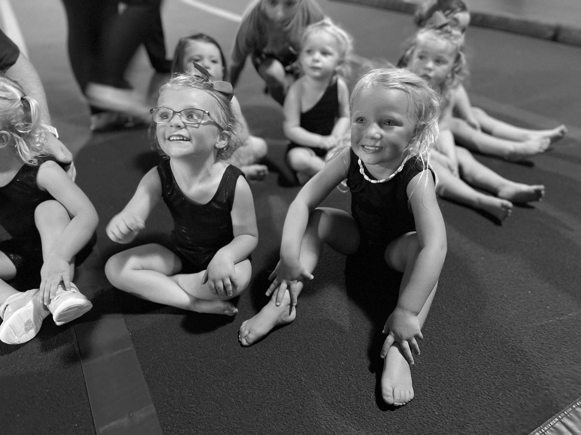 A group of young girls are sitting on the floor in a gym.