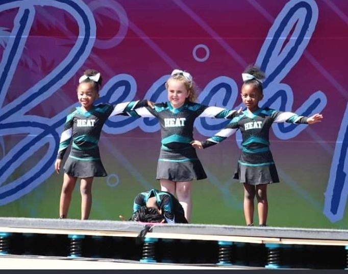 Three cheerleaders are standing on a stage wearing shirts that say heat