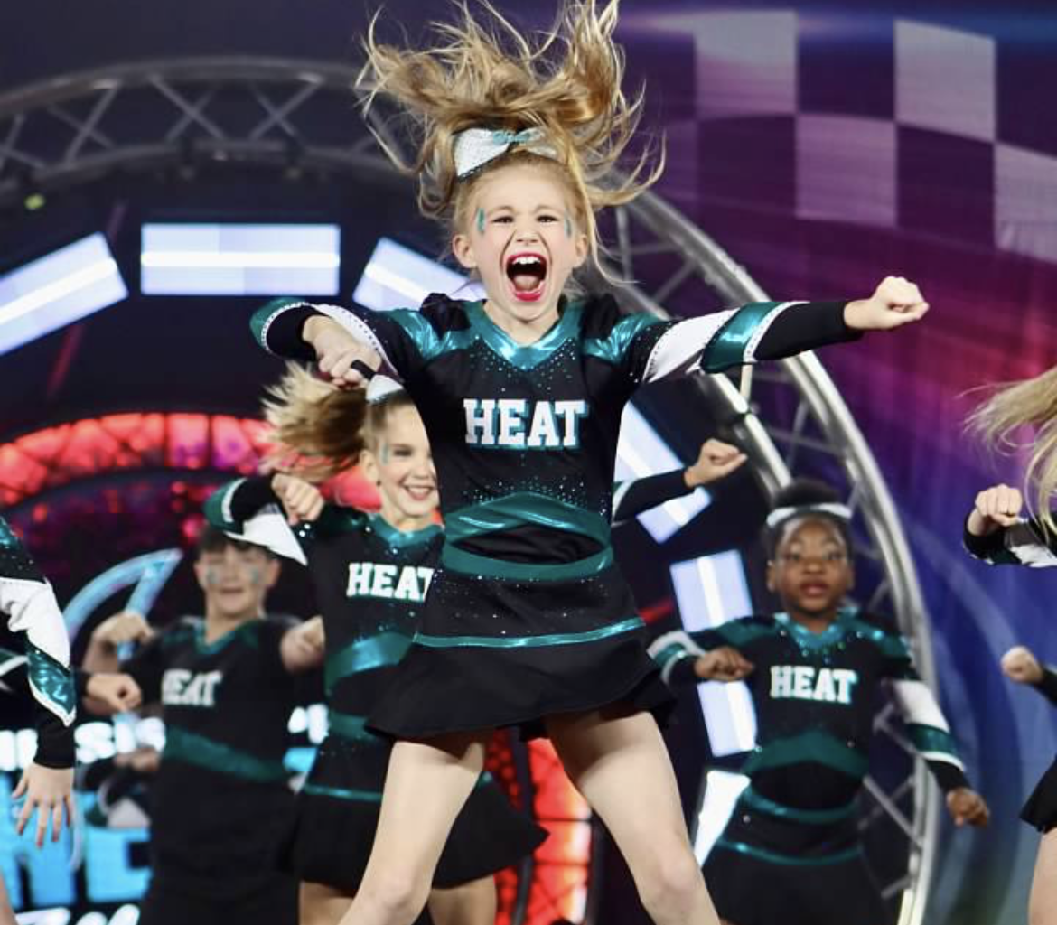 A girl in a heat cheerleading uniform is jumping in the air