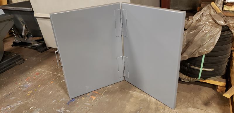 Two gray folding panels on a concrete floor in a warehouse setting.