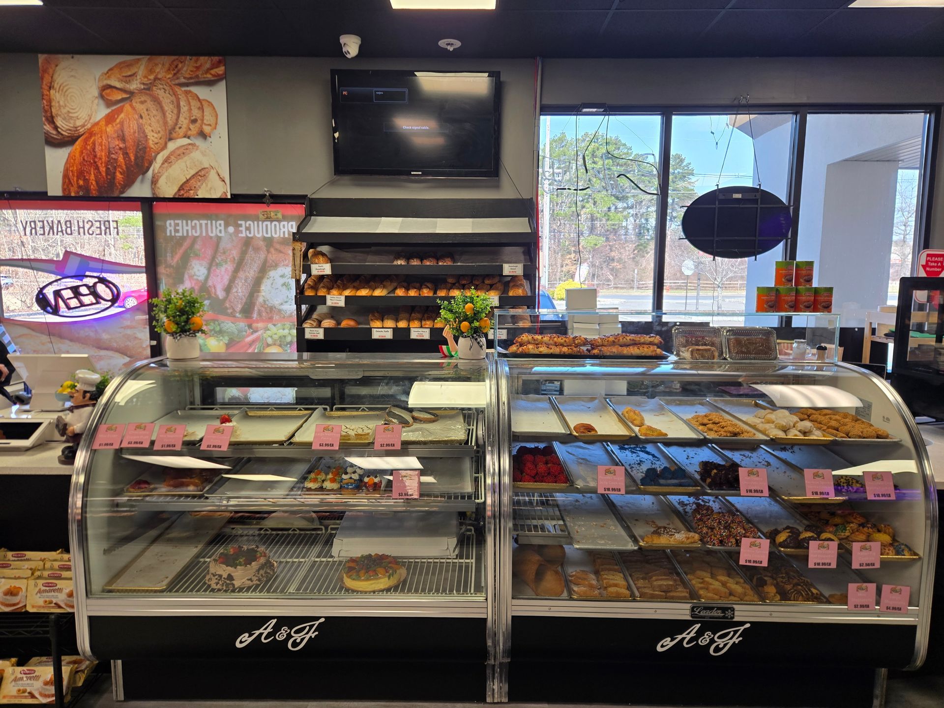 Bakery counter with glass display cases, pastries, and a menu screen in a bright shop.