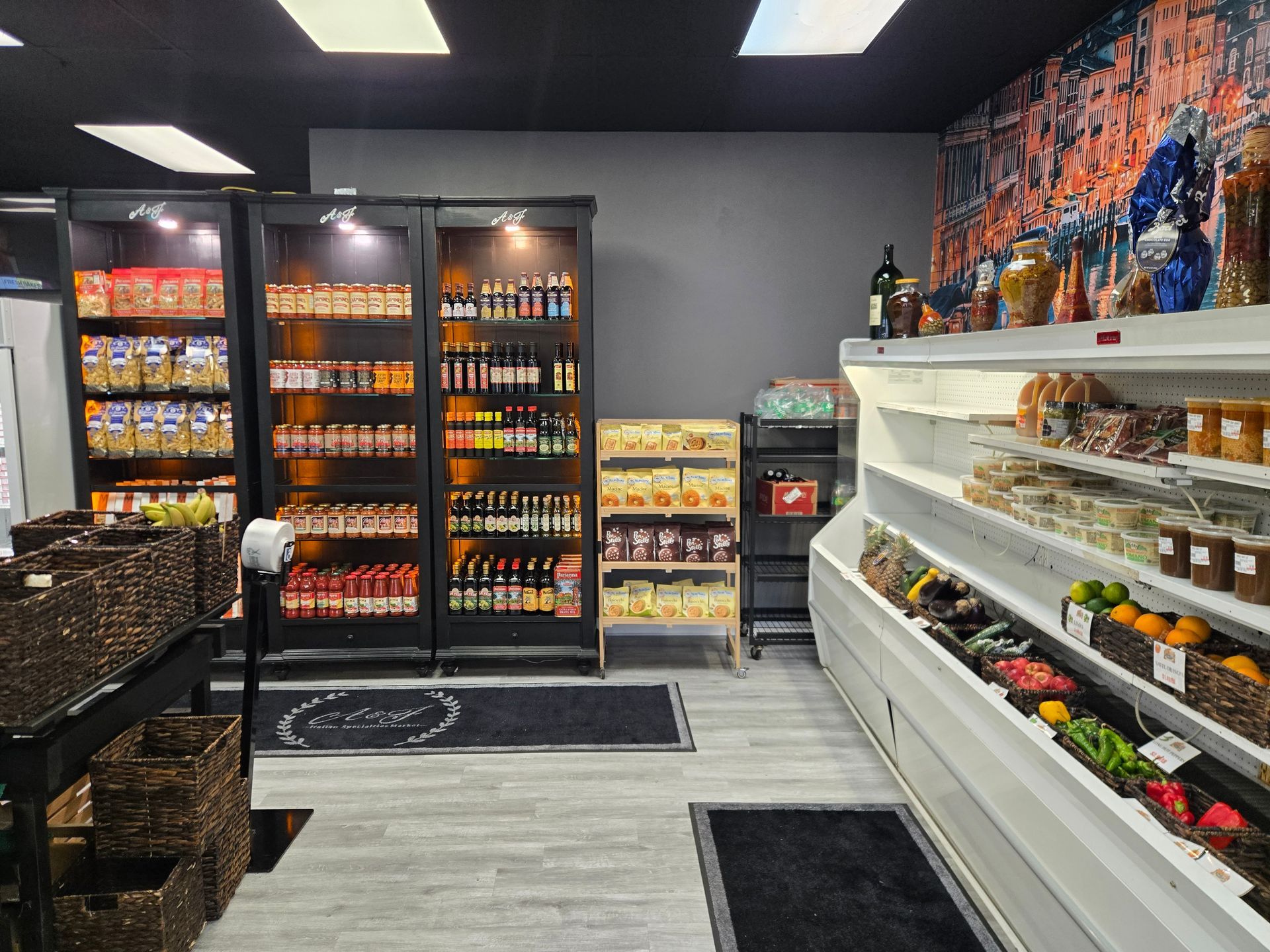 Small convenience store aisle with refrigerated drinks, snacks, and produce displays under bright lights.
