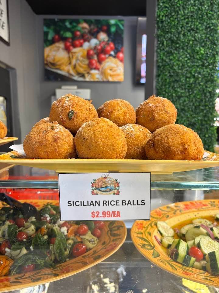 Tray of golden Sicilian rice balls with price sign at a deli counter