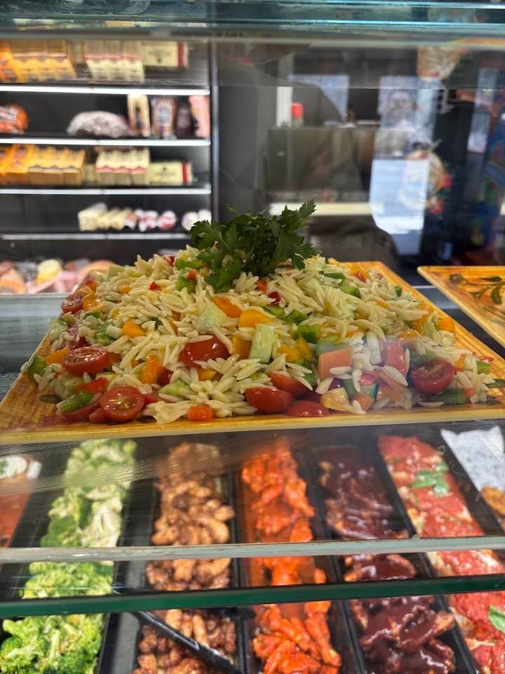 Tray of colorful salad in a deli display case with shelves of food behind it