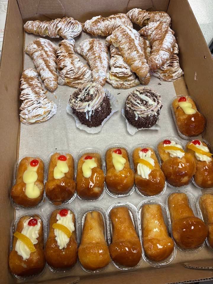 Assorted pastries and donuts in a box, some powdered and filled with cream and jam.