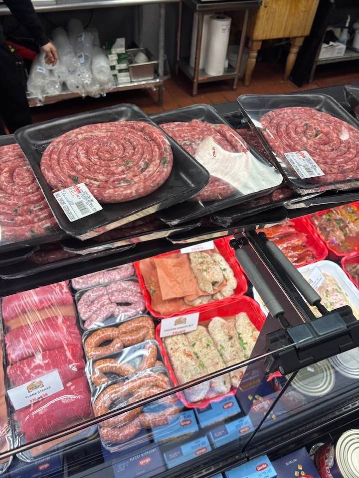 Meat counter with trays of sausages, bacon, and packaged deli items in a grocery store display.