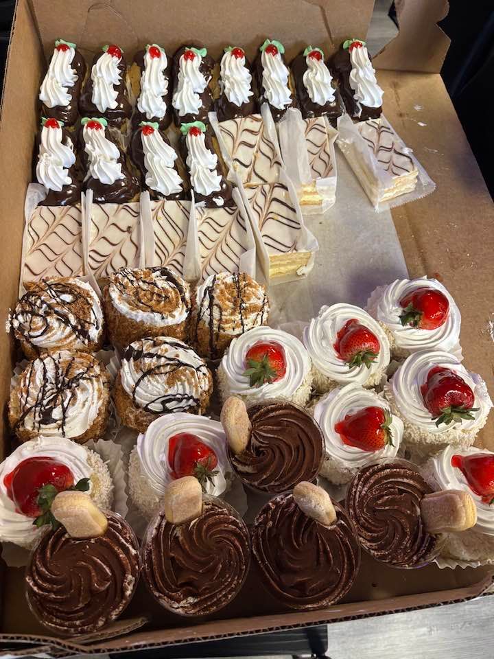 Tray of assorted decorated pastries with whipped cream, chocolate swirls, and strawberries in a bakery box