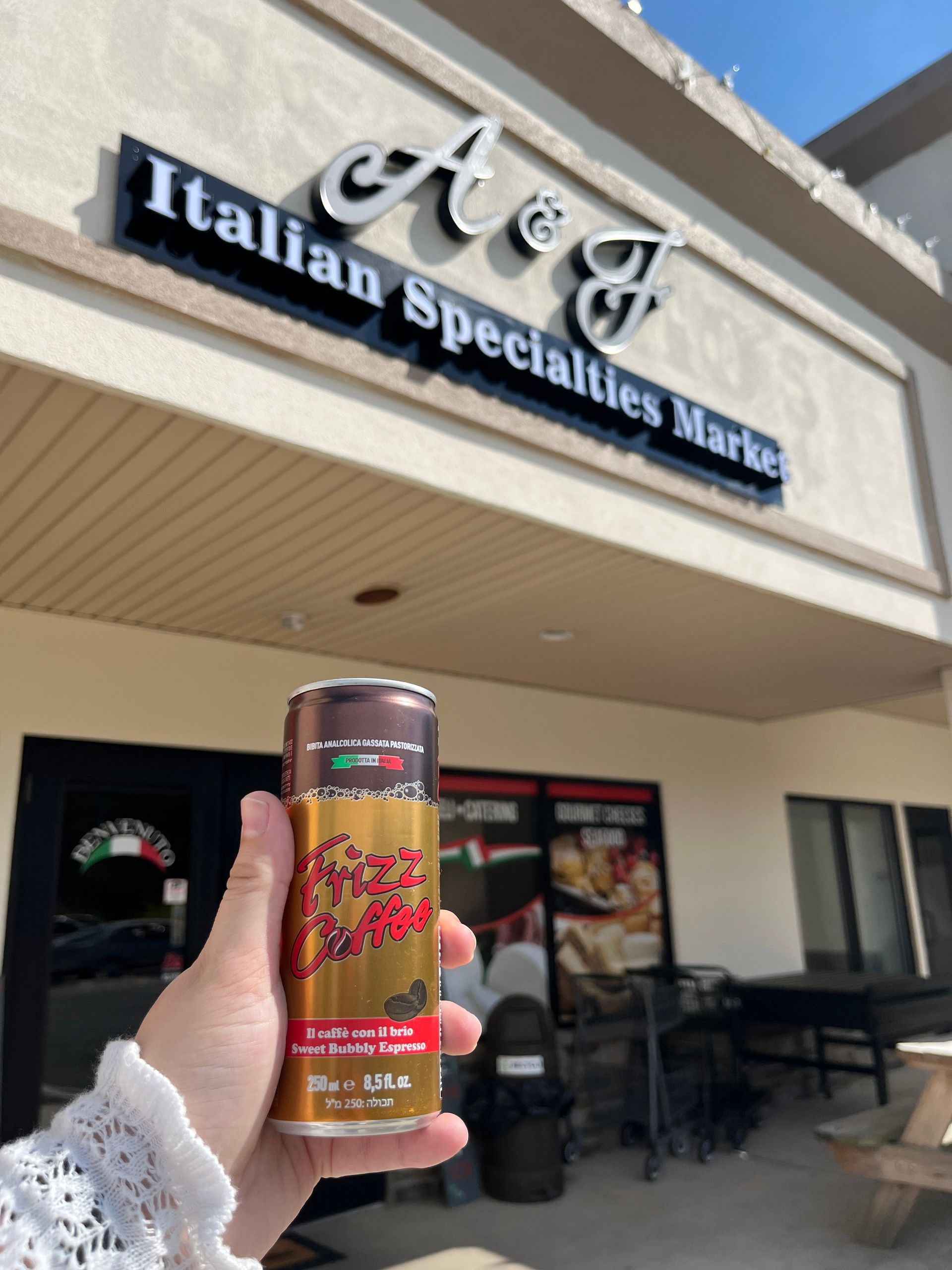 Hand holding a colorful energy drink can in front of a market storefront sign.