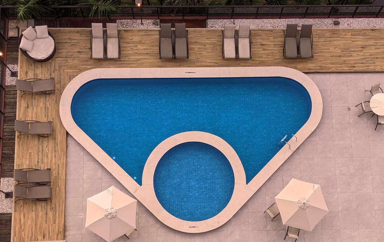 Vista aérea: área da piscina com água azul, espreguiçadeiras e guarda-sóis.