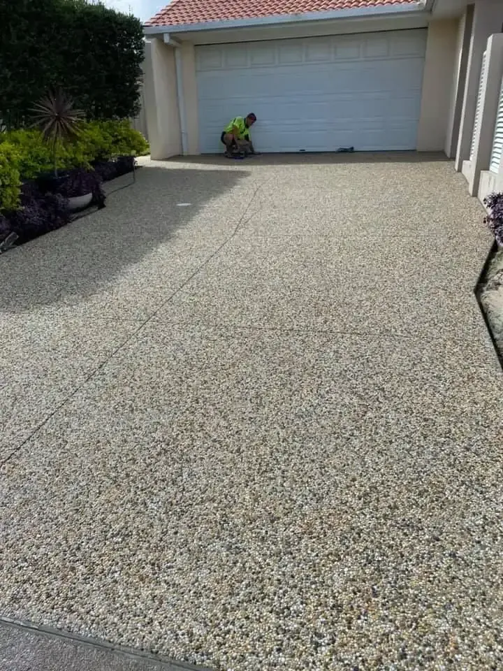 A Man Is Cleaning A Driveway In Front Of A Garage Door — Luke Seears Concreting in Port Macquarie, NSW