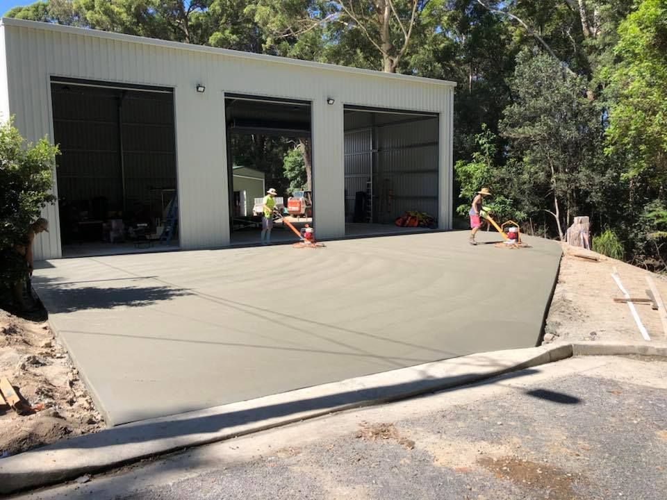 A Man Is Working On A Concrete Driveway In Front Of A Garage — Luke Seears Concreting in Port Macquarie, NSW