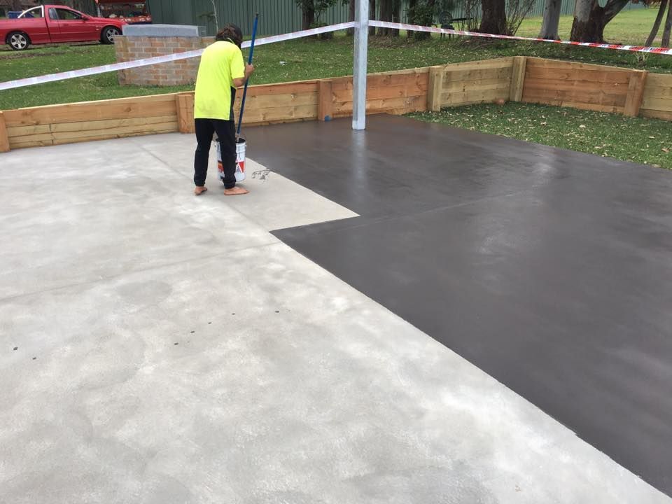 A Man Is Painting A Concrete Driveway With A Sprayer — Luke Seears Concreting in Wauchope, NSW