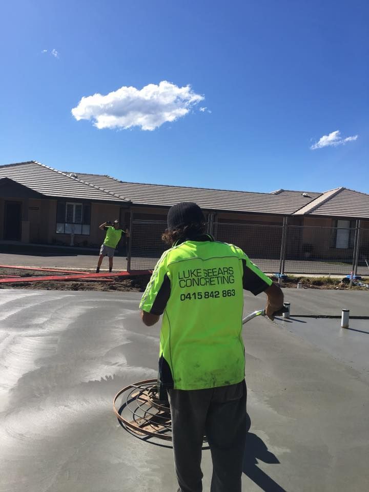 A Man Is Working On A Concrete Floor In Front Of A House — Luke Seears Concreting in Wauchope, NSW