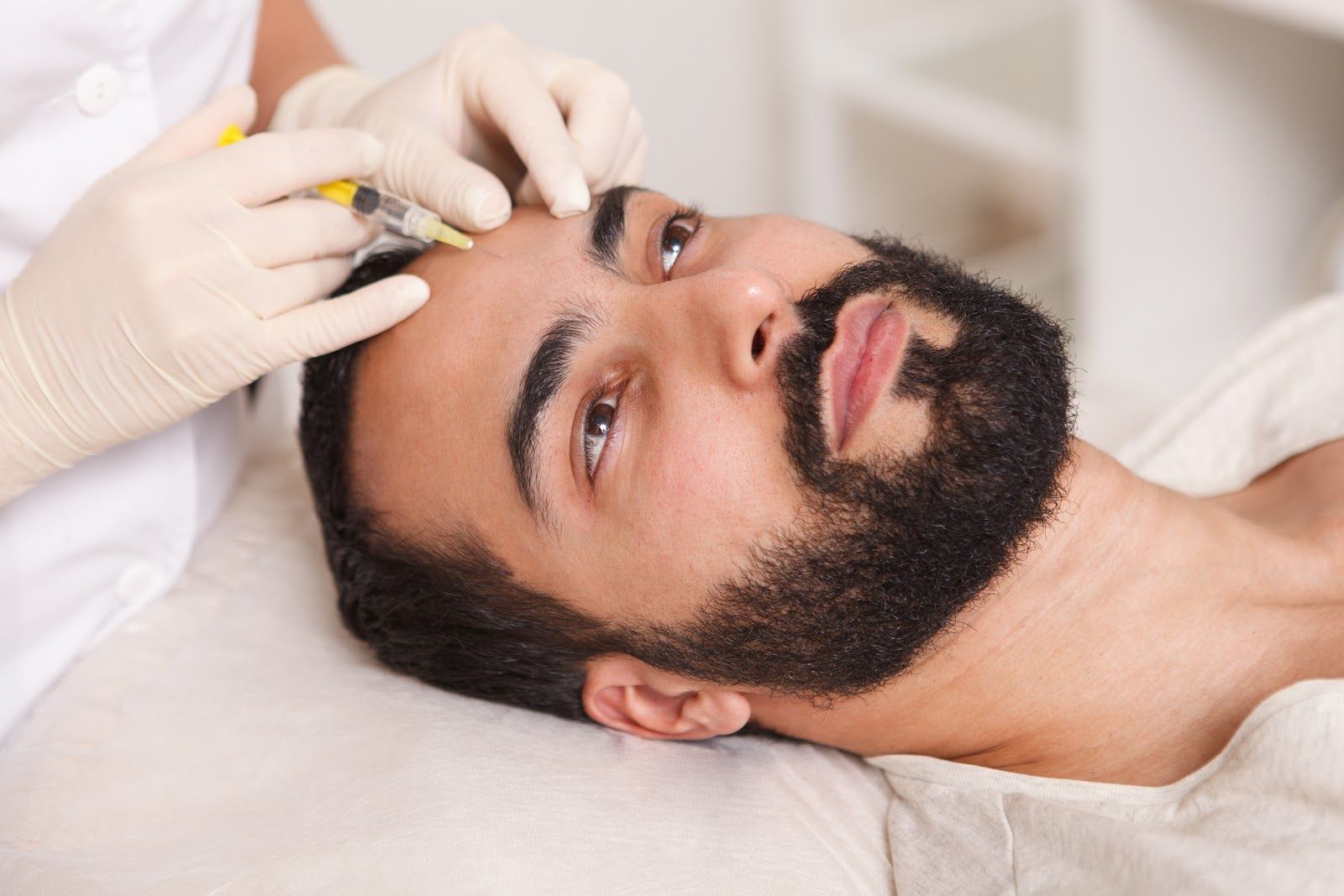 Gloved hands applying eyebrow treatment to a reclining man in a spa setting