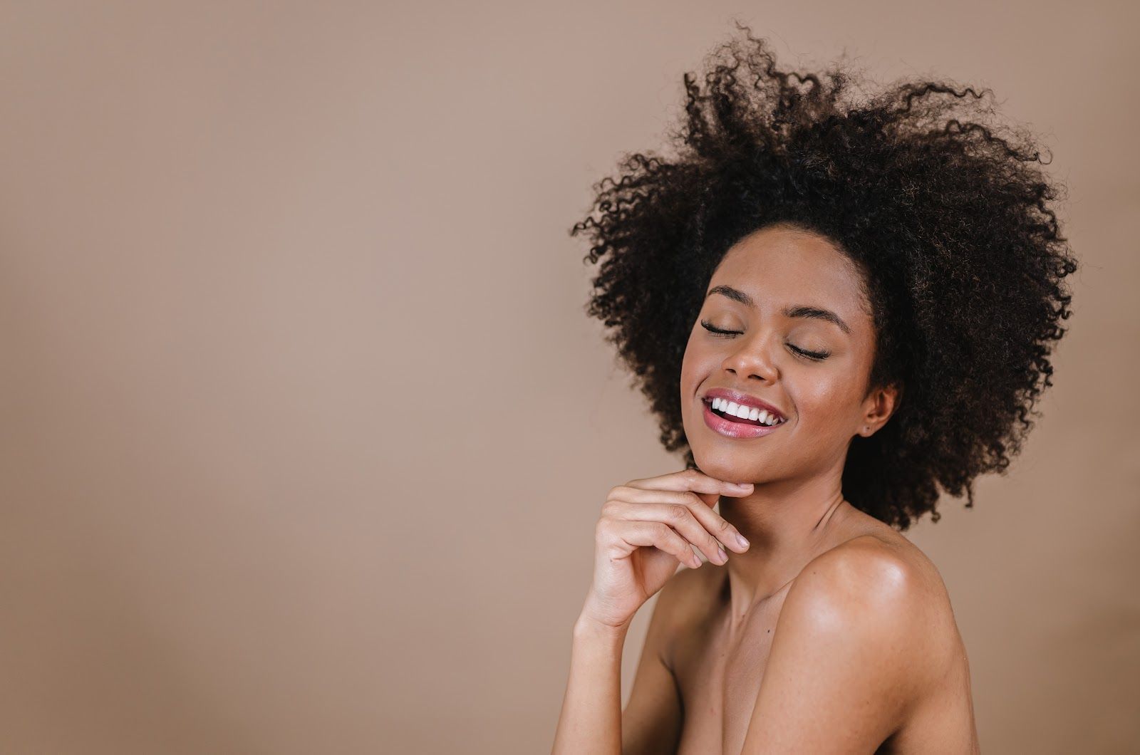 Smiling person with curly hair posing against a beige background