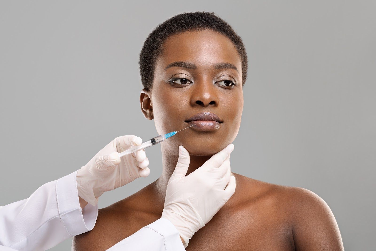 Medical professional preparing an injection in a woman's face against a gray background