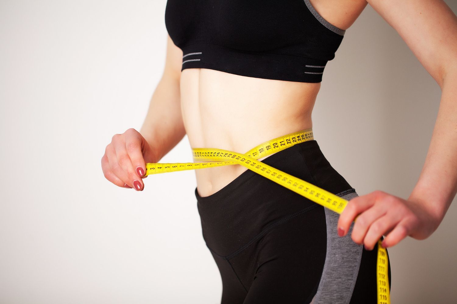 Person measuring waist with a yellow tape measure, wearing black workout clothes.