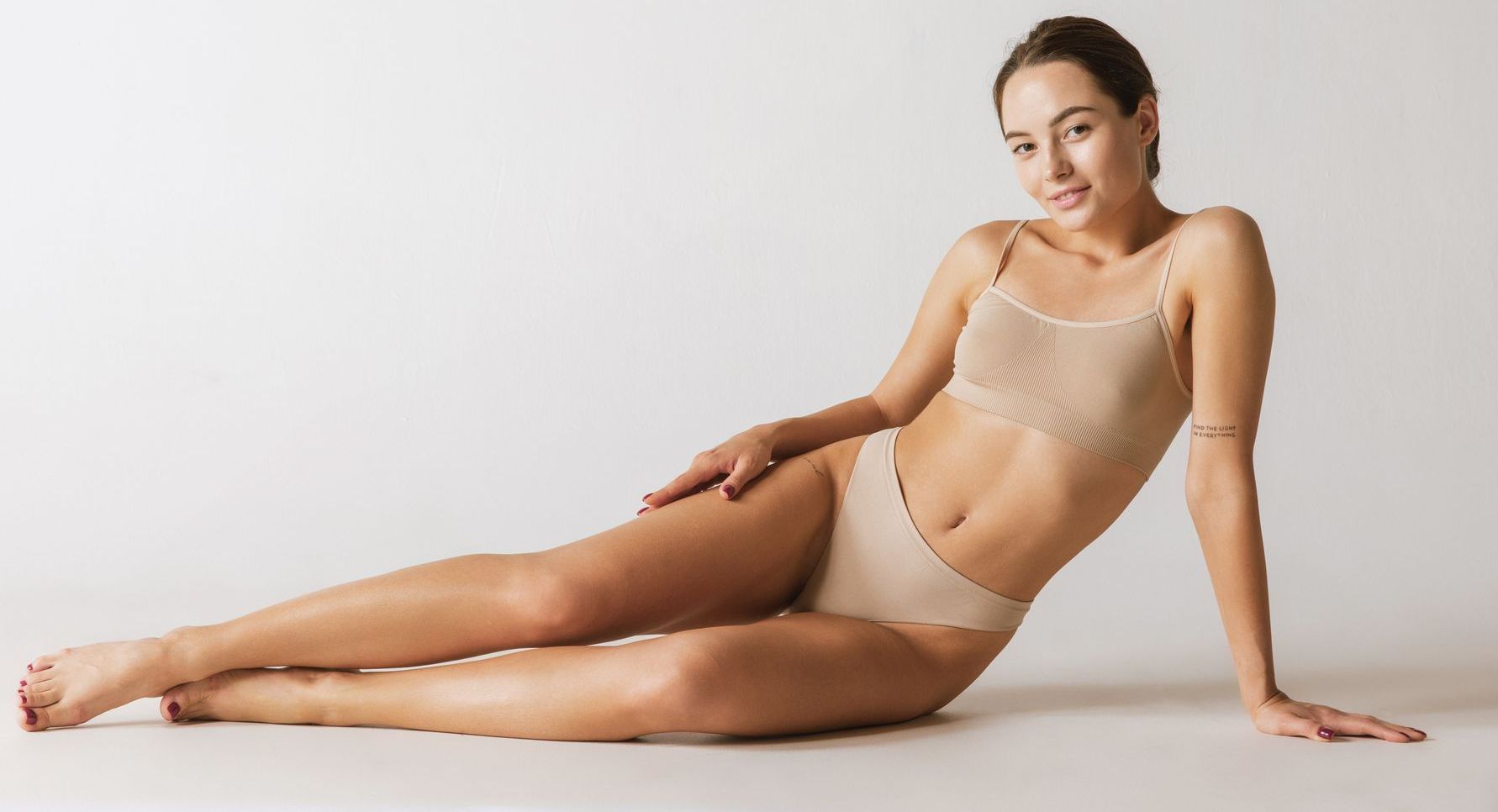 A woman in lingerie is sitting on the floor with her legs crossed.