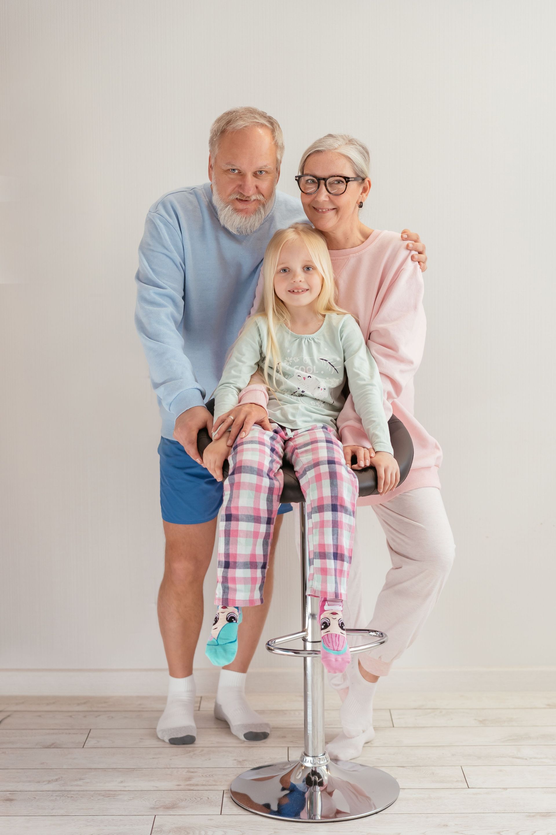 Three smiling people posed on a stool in a bright studio, with a child seated between two adults