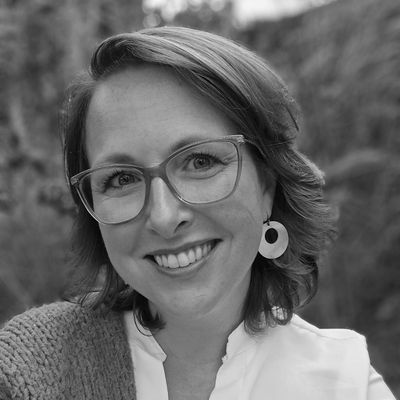 Een vrouw met een bril en oorbellen lacht op een zwart-witfoto.