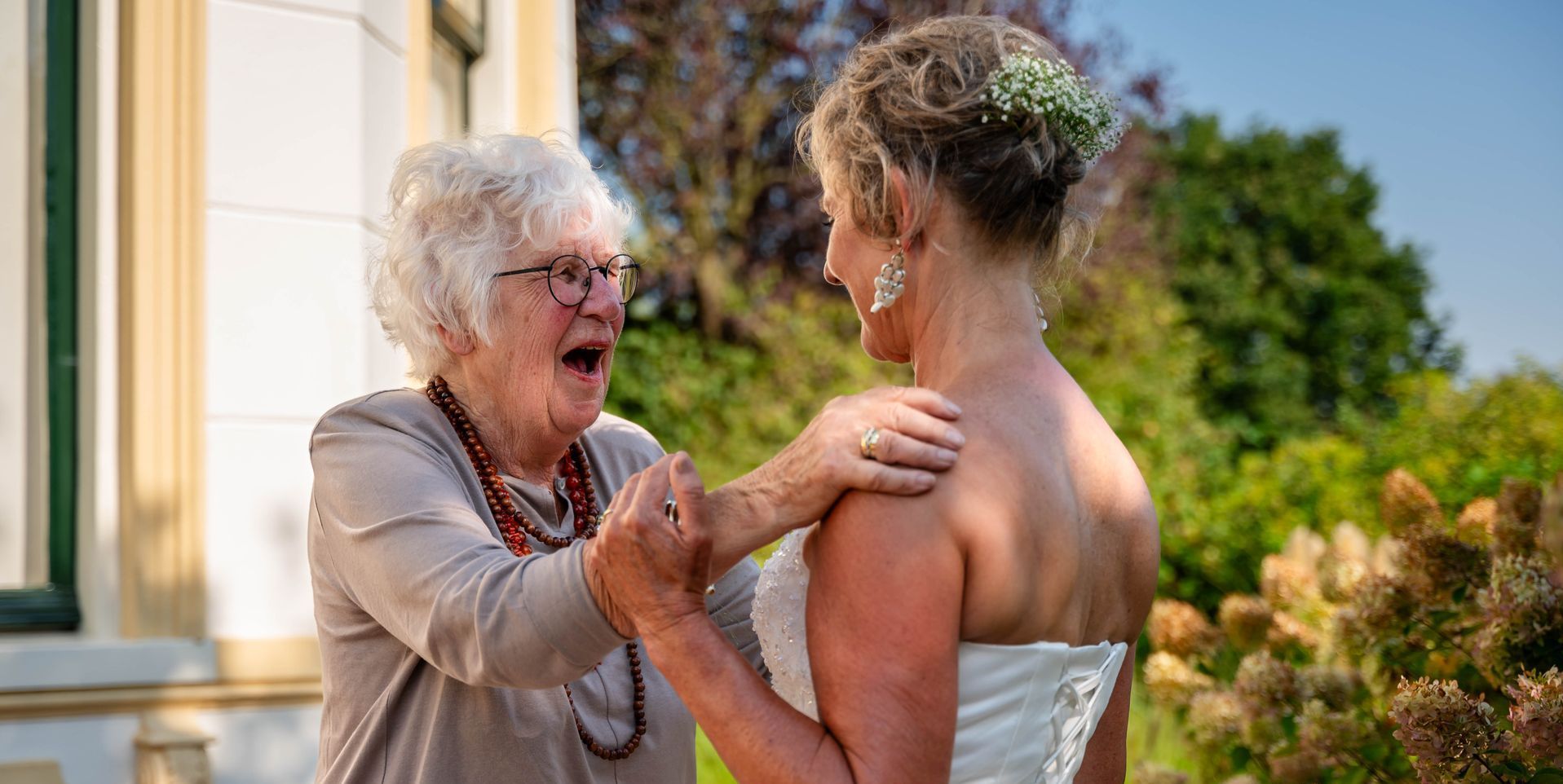 Een oudere vrouw omhelst een bruid in een trouwjurk.
