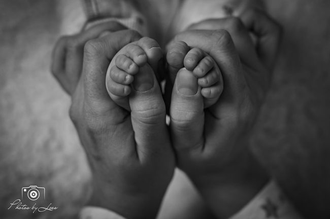 Een zwart-witfoto van een persoon die de voeten van een baby vasthoudt.