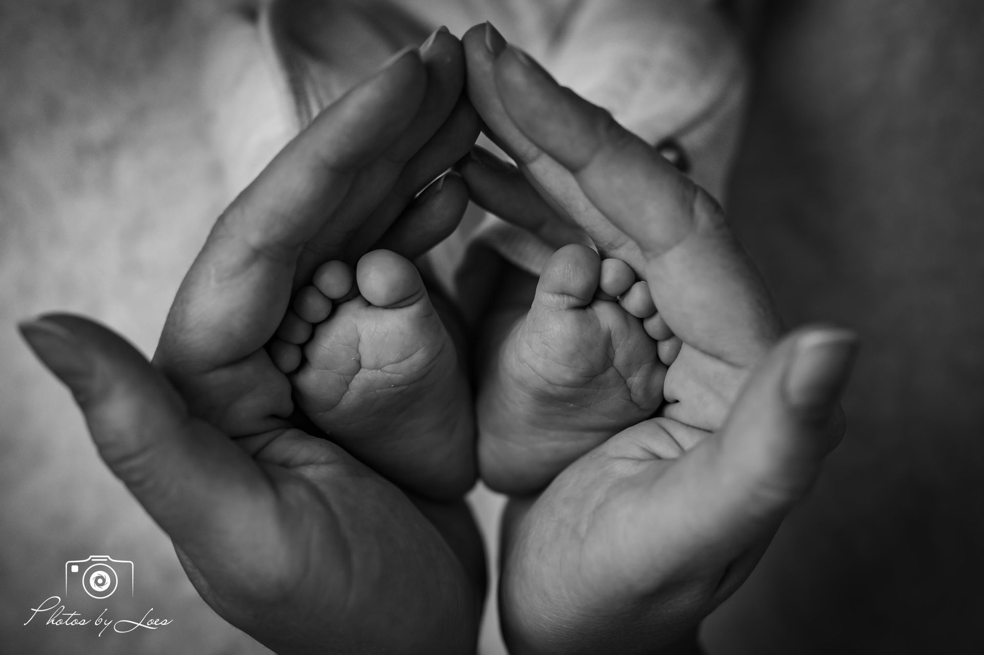 Op een zwart-witfoto houdt een vrouw de voeten van een baby in haar handen.