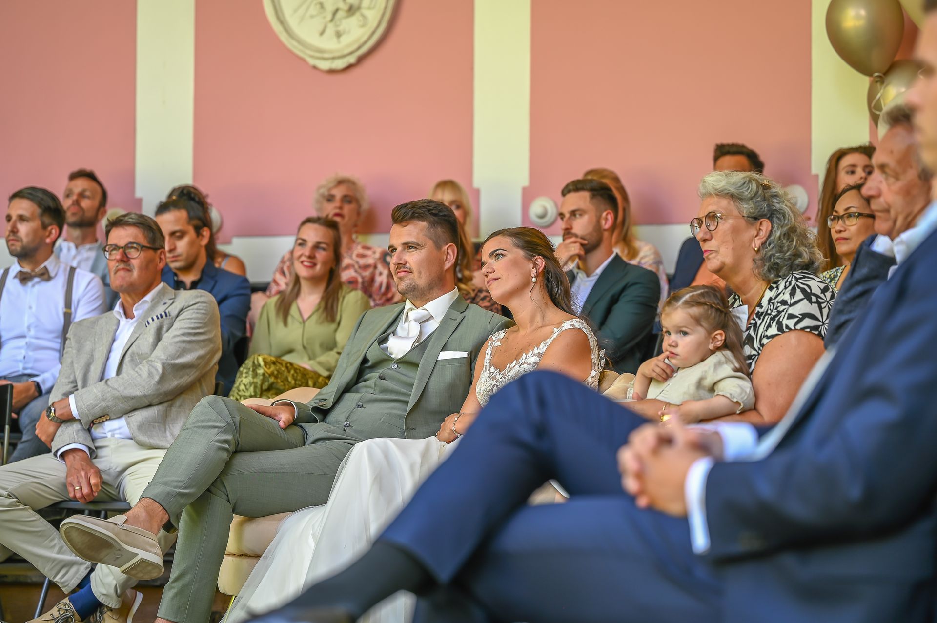 Een groep mensen zit in een kamer en kijkt naar een huwelijksceremonie.