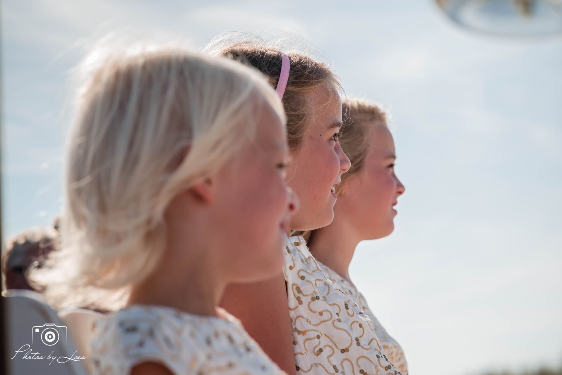 Drie kleine meisjes staan ​​naast elkaar en kijken naar de camera.