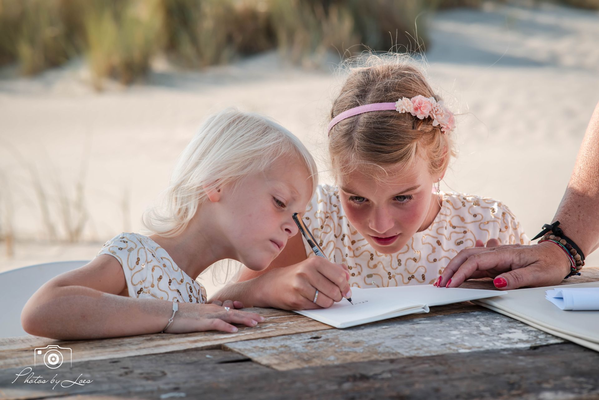 Twee kleine meisjes zitten aan een tafel en schrijven in een notitieboekje.
