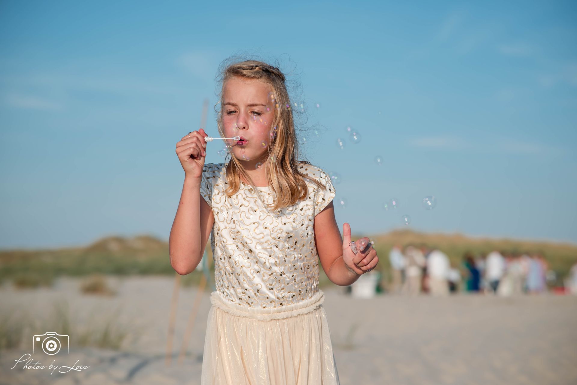 Een klein meisje blaast zeepbellen op het strand.