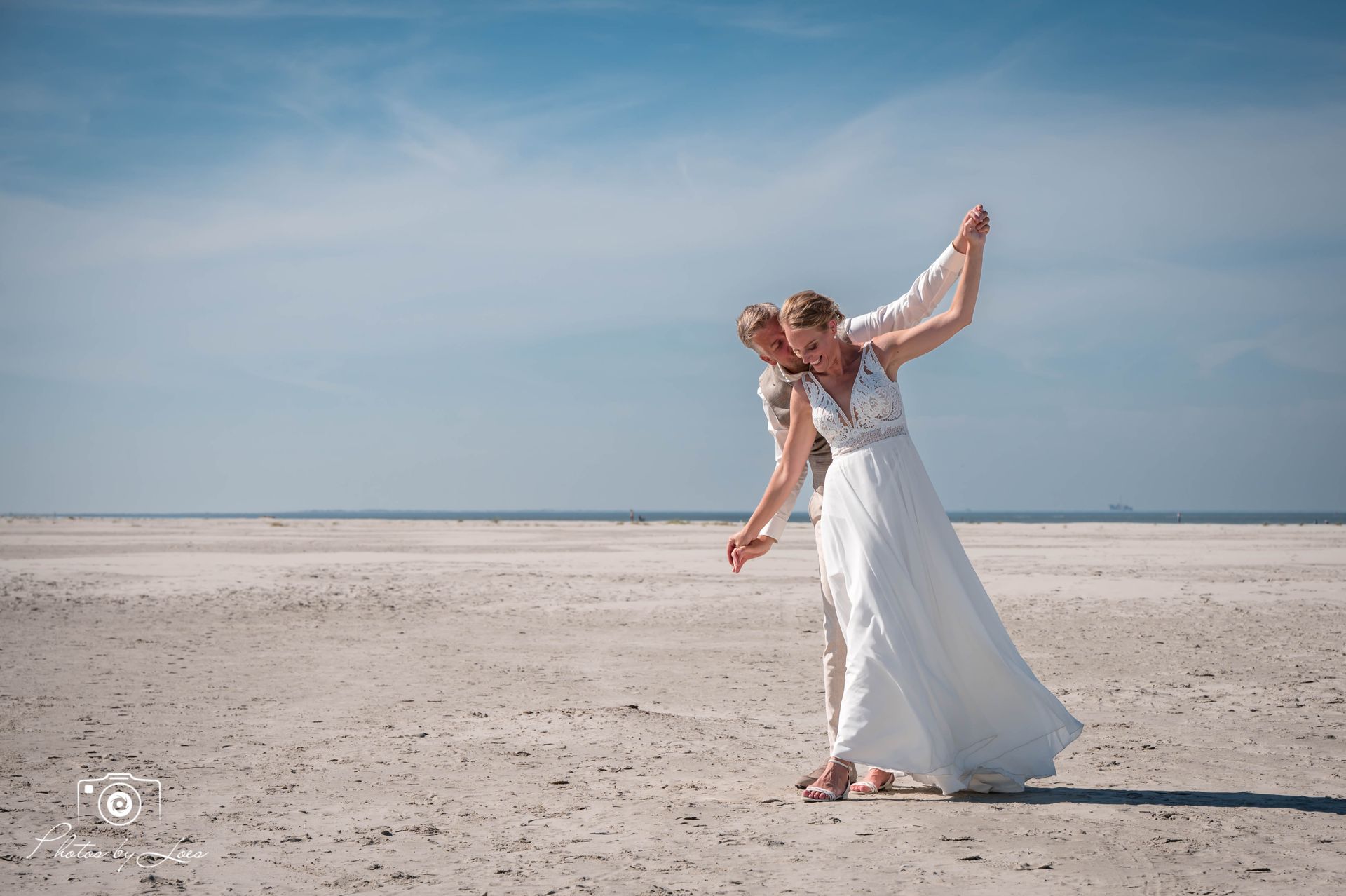 Een bruid en bruidegom dansen op het strand.