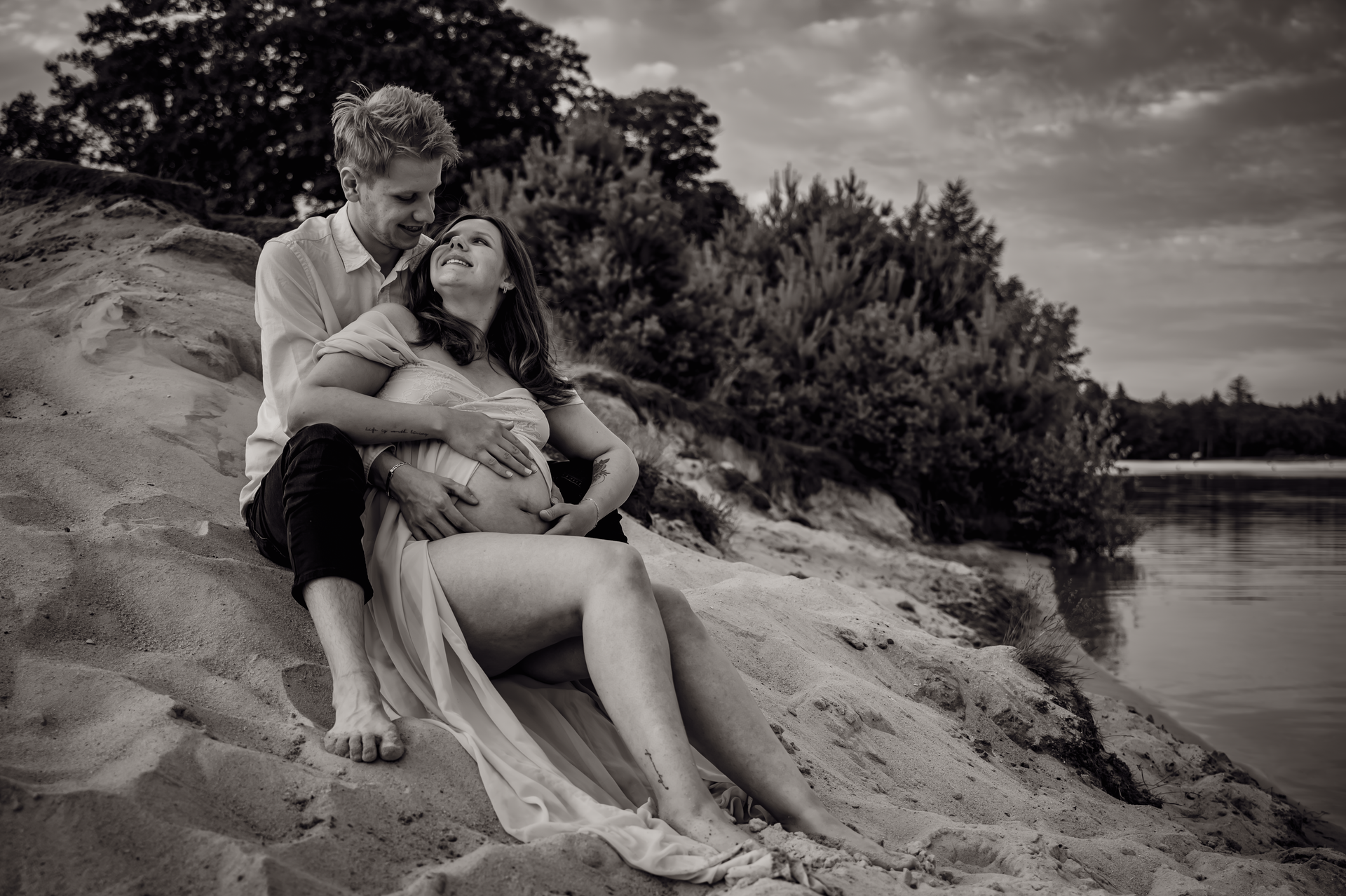 Een man en een zwangere vrouw zitten op een zandstrand.