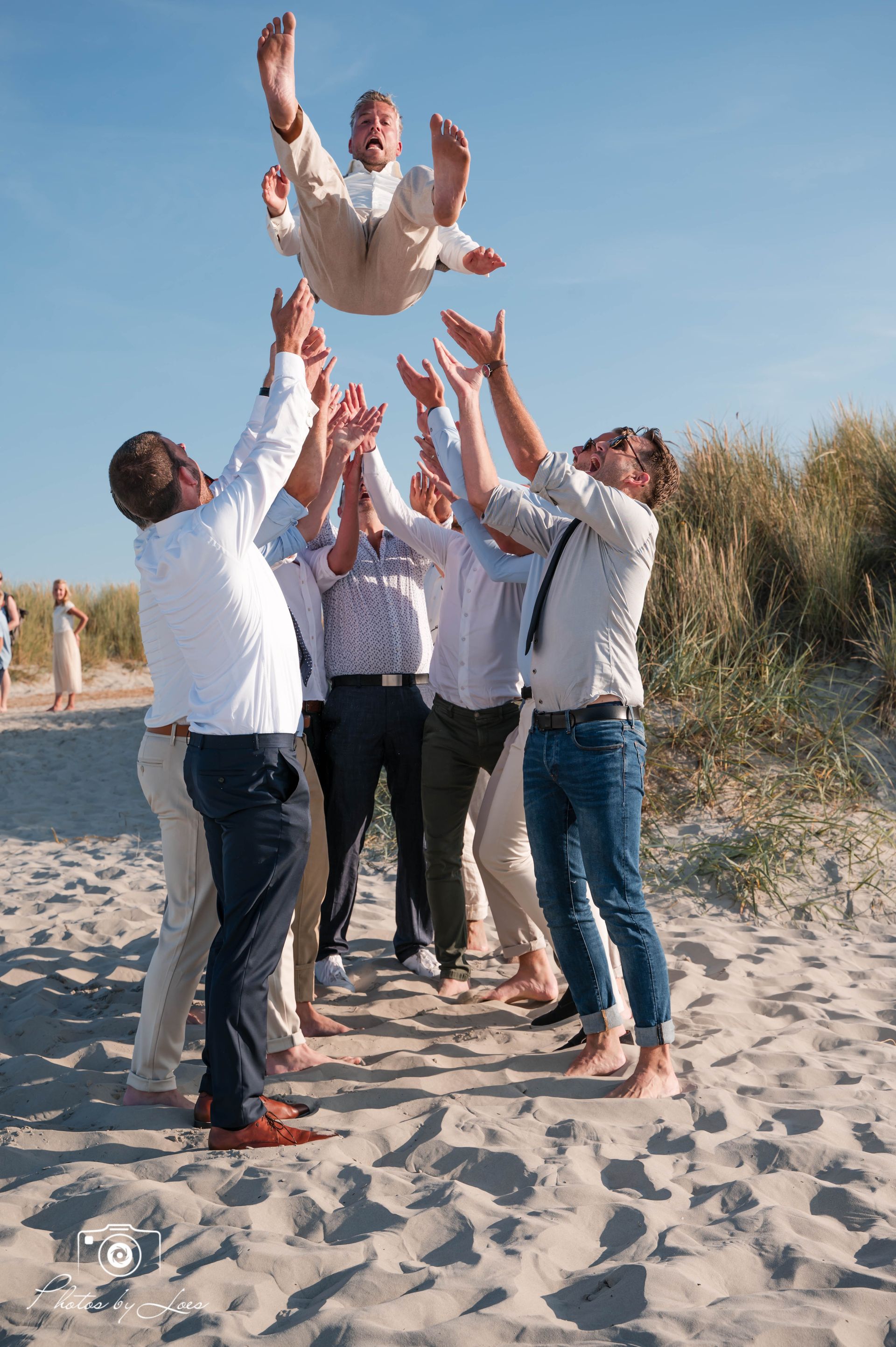 Een groep mannen staat op het strand en houdt een man in de lucht.