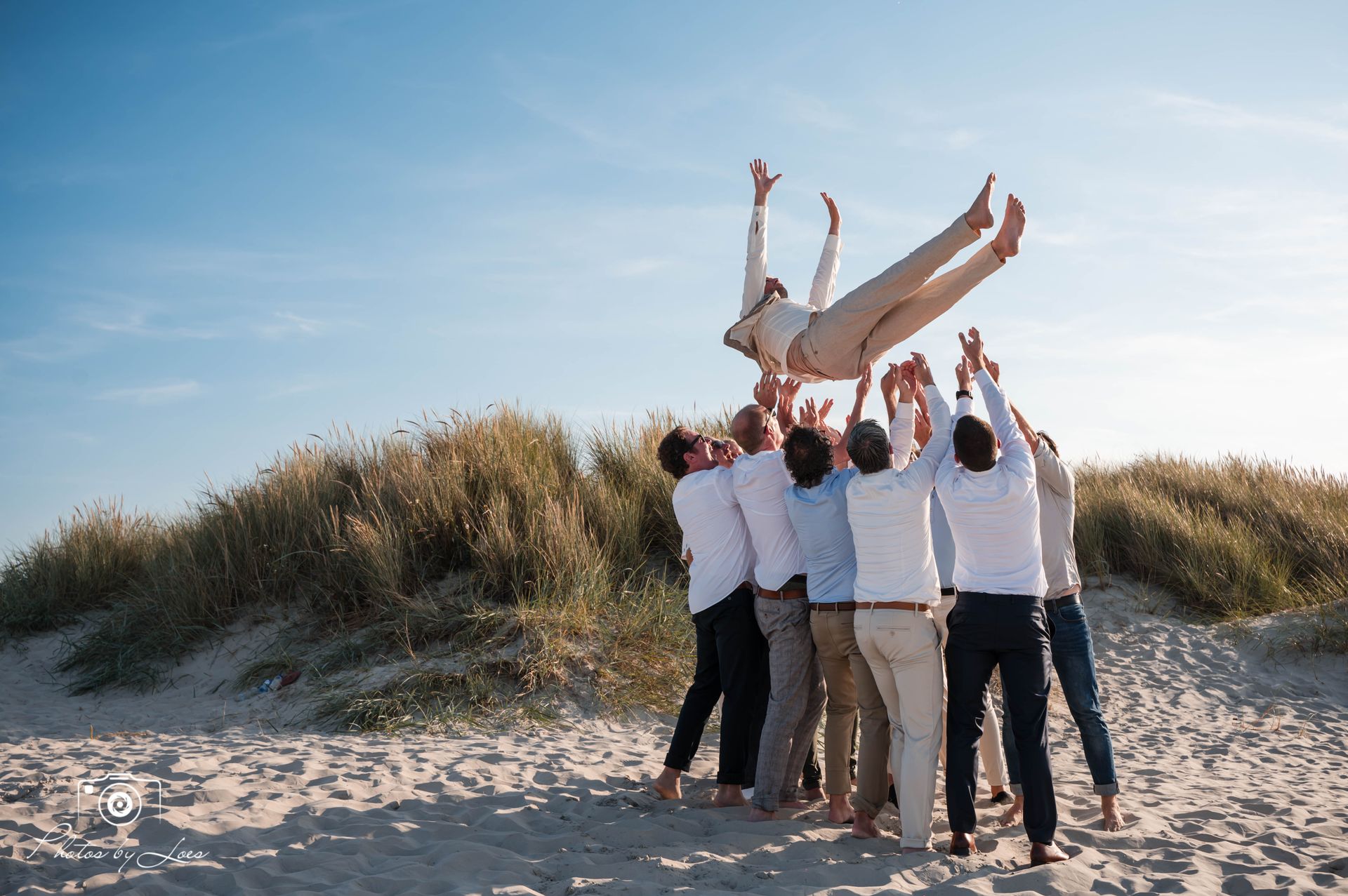 Een groep mannen houdt een man in de lucht op een strand.