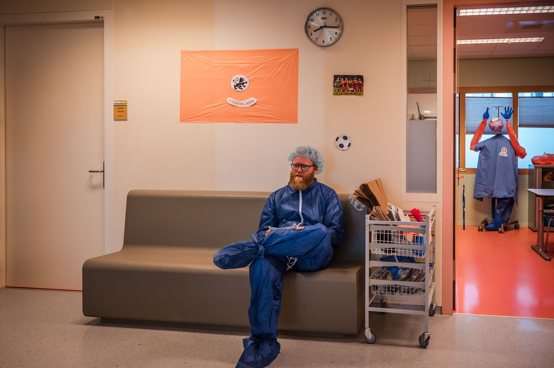Een man in een laboratoriumjas zit op een bank in een wachtkamer.