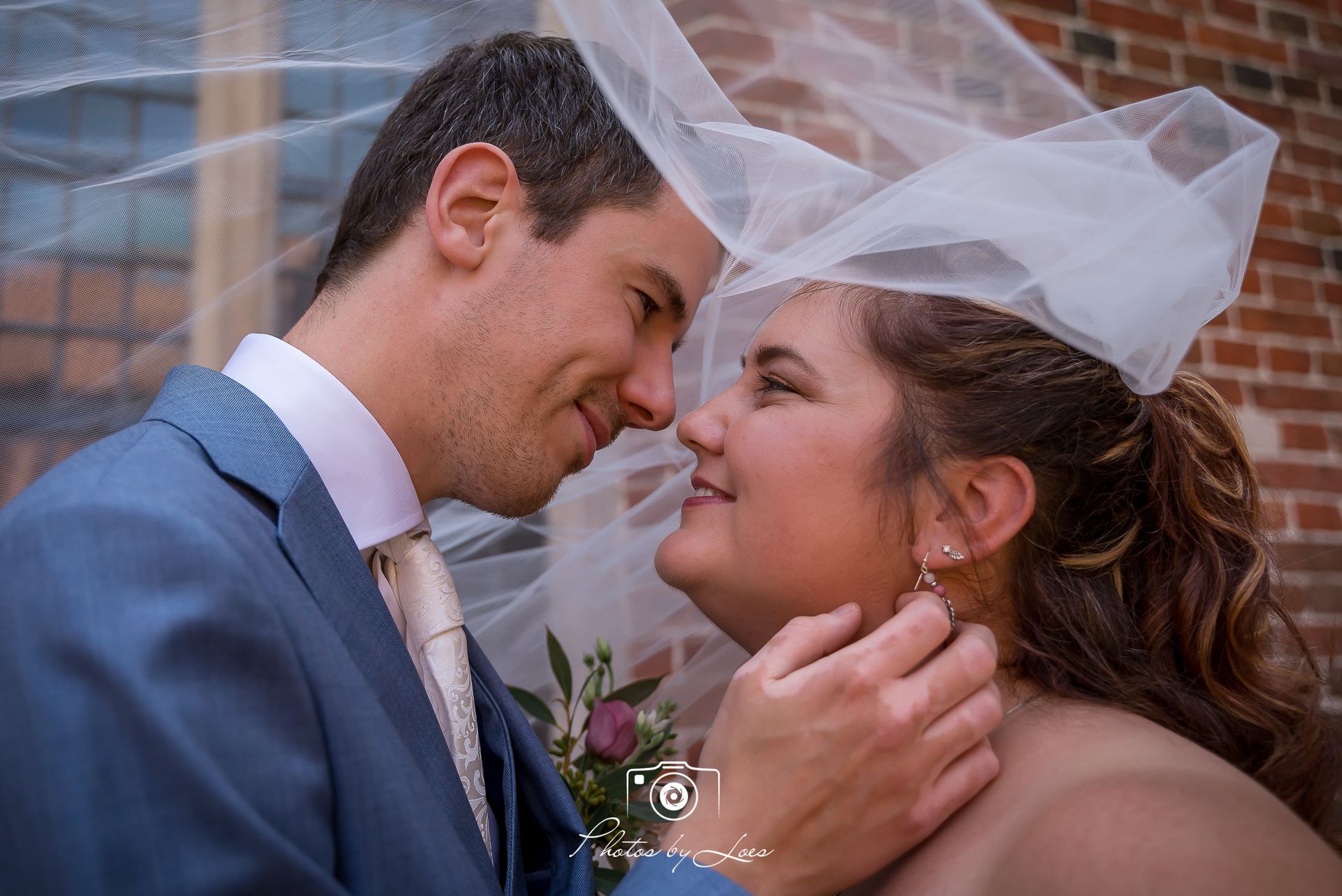 Een bruid en bruidegom kijken elkaar aan, terwijl hun sluier in de wind wappert.