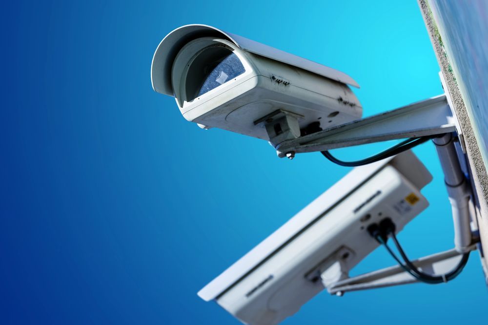 Dos cámaras de seguridad blancas montadas sobre un fondo de cielo azul.