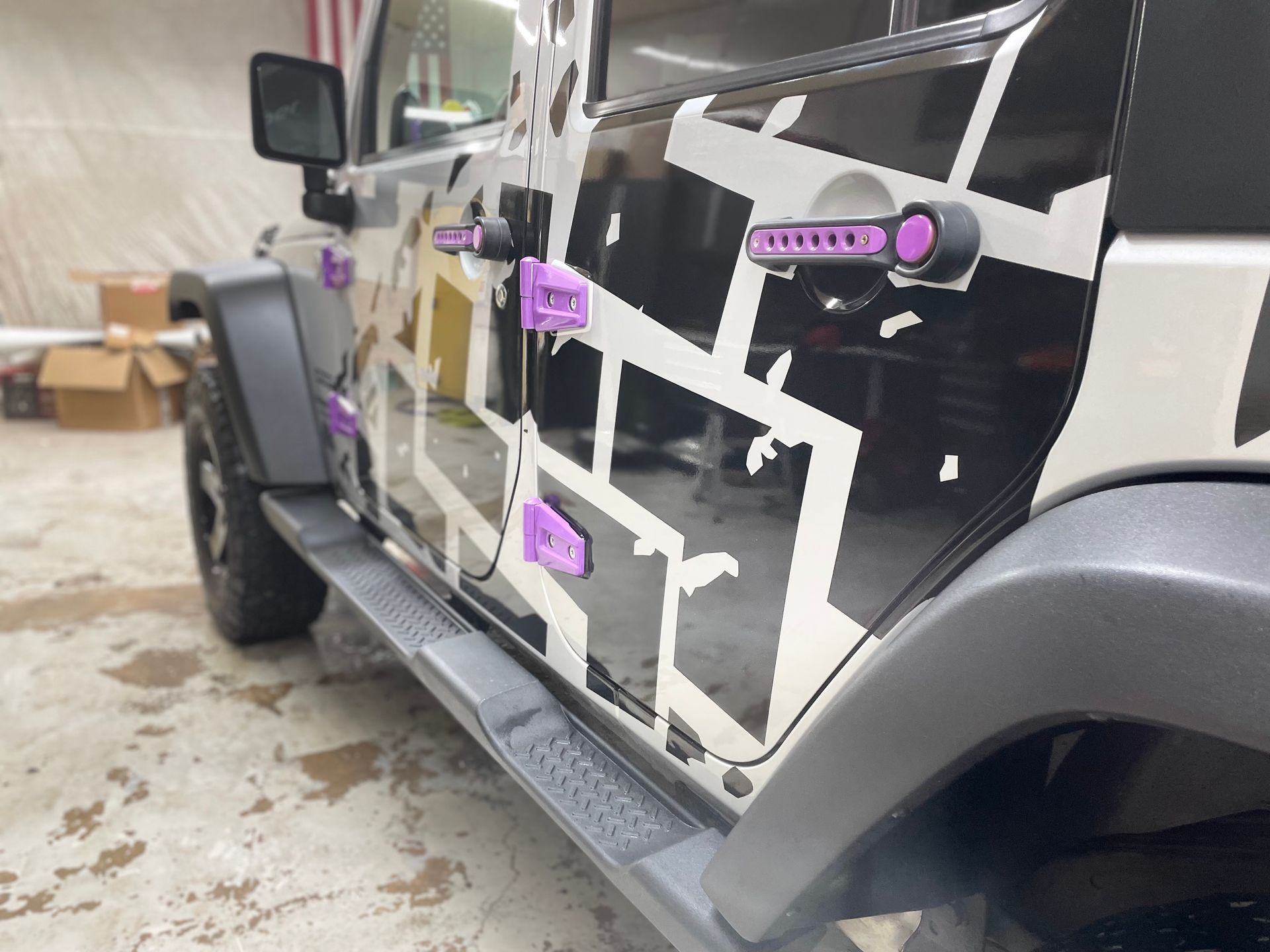 A black and white jeep with purple handles is parked in a garage.