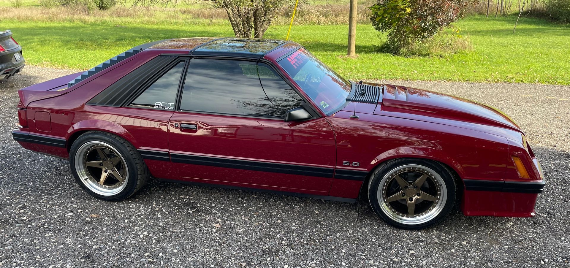 A red mustang is parked in a gravel driveway.