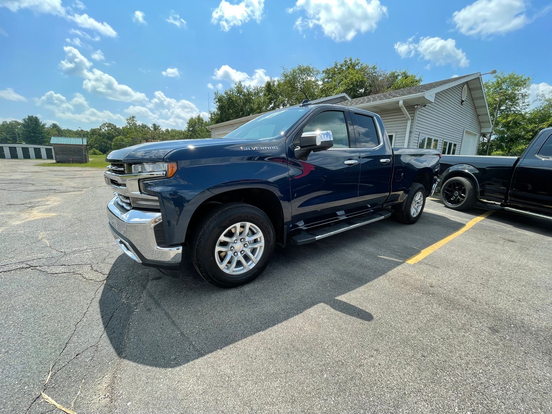 A blue truck is parked in a parking lot next to a black truck.