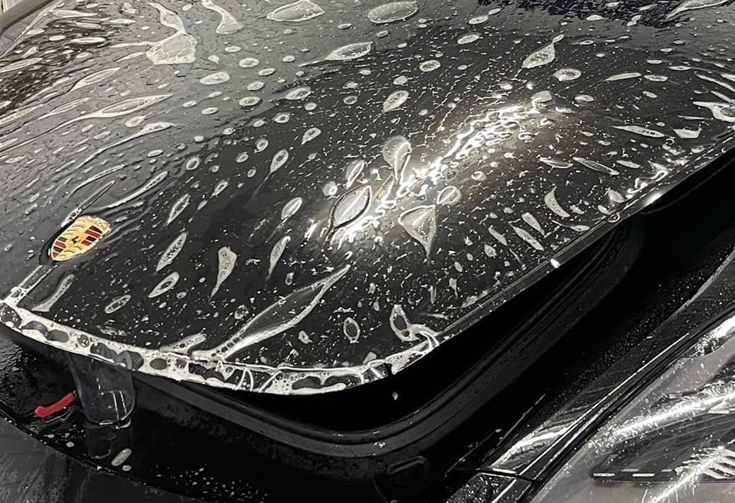 A close up of a black car with water drops on it.
