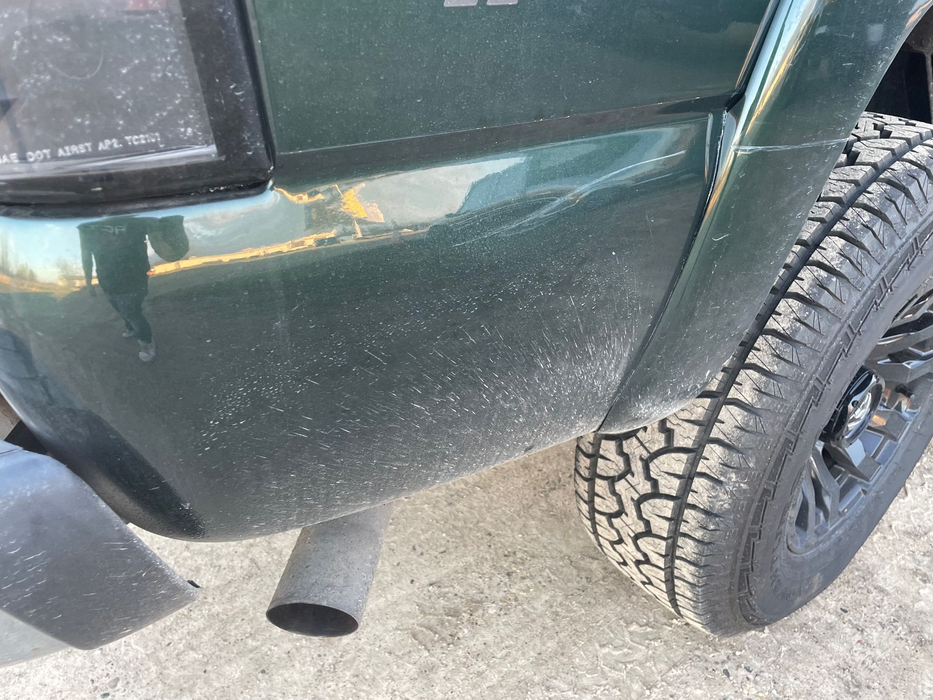 A close up of a green truck 's bumper and tire