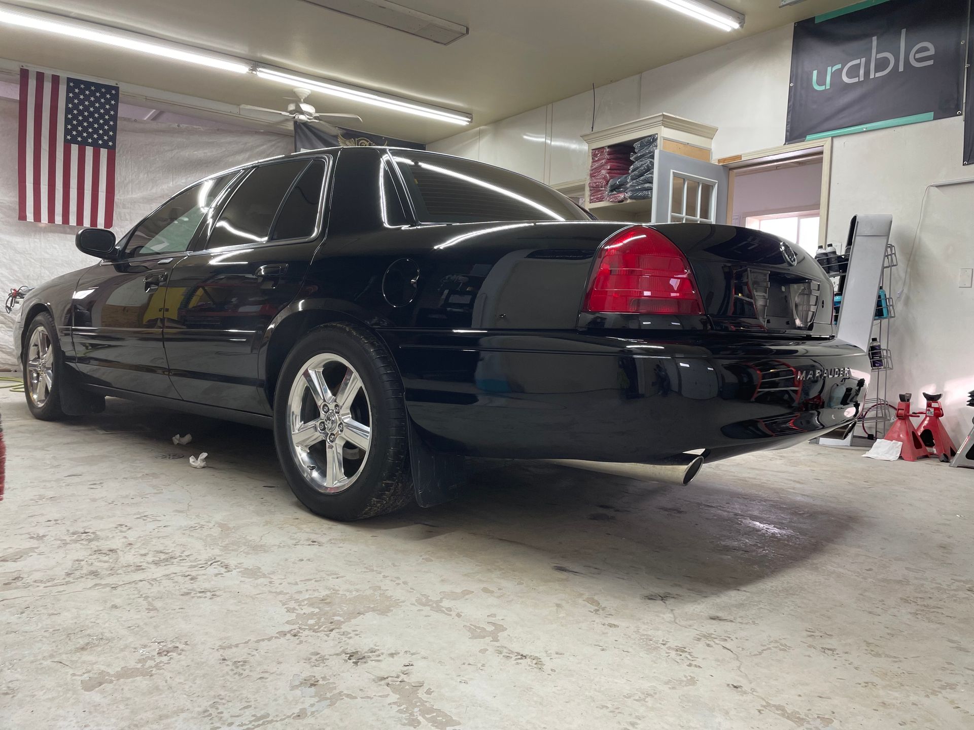 A black car is parked in a garage next to an american flag.