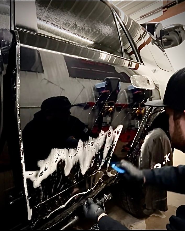 A man wearing black gloves is working on a black car